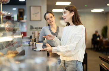 Two young women friends drinking coffee and talking at counter in cafe