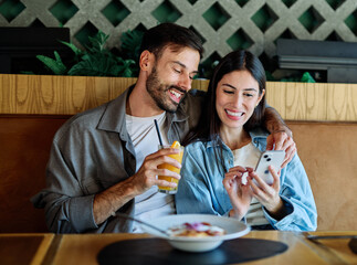 Portrait of ayoung romantic couple in restaurant having lunch and using a mobile phone