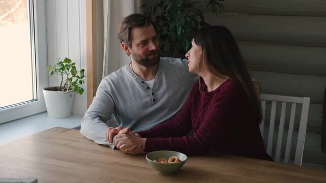 Loving mature couple interactions at home. Husband and wife hugging, holding hands and drinking morning coffee together. Man and woman talk about plans for weekend. Natural lighting. Intimate moments.