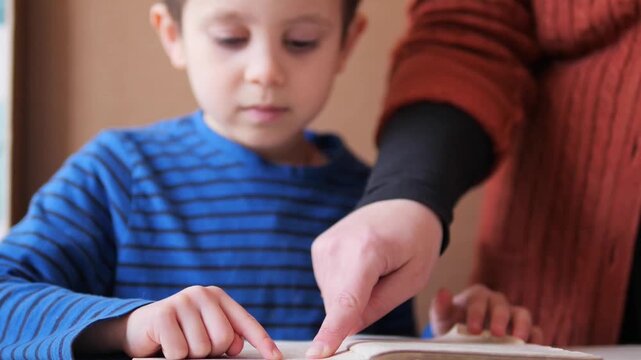 Mother pointing at words in a book for a young boy - collaborative reading and mentorship during a home education lesson
