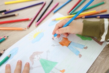 Naklejka premium Little boy drawing with pencil at wooden table, closeup