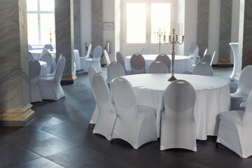 Naklejka premium Elegant banquet hall white tables covered chairs classic candelabra creates refined atmosphere wedding formal event. Marble columns soft daylight symmetry luxury order timeless interior design