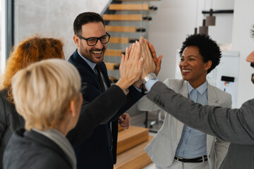 A diverse team of successful business professionals celebrating a victory in a modern office. They...