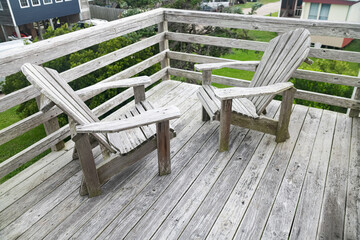 Empty adirondack chairs on wooden patio deck with railing and natural daylight