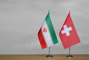 Two table flags of Iran and Switzerland on a blurred gray background