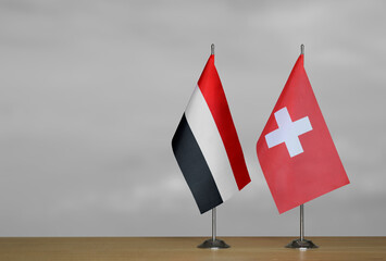 Two table flags of Yemen and Switzerland on a blurred gray background