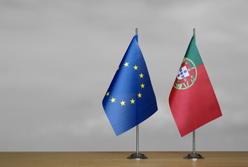 Two table flags of the European Union and Portugal on a blurred gray background