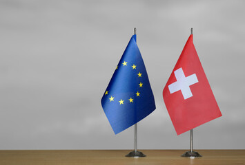 Two table flags of the European Union and Switzerland on a blurred gray background