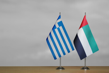 Two table flags of Greece and Emirates on a blurred gray background