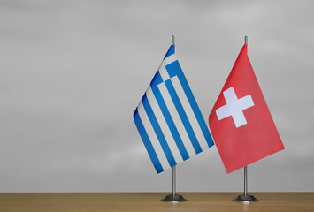 Two table flags of Greece and Switzerland on a blurred gray background