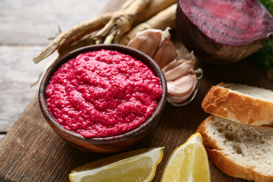 Bowl of horseradish sauce with beet, bread and lemon on wooden background, closeup