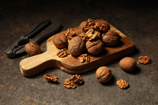 Wooden board with walnuts and nut cracker on grey grunge background