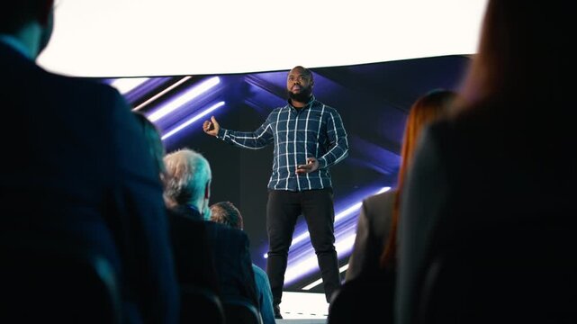 Black chief product officer introducing new smartphone with modern interface and design for marketing announcement. Mixed age audience during launch event focused on release. Camera A.