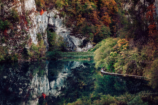 View of tranquil waters mirroring the colorful autumn foliage along rocky cliffs and a wooden path, Plitvicka Jezera, Lika-Senj County, Croatia.