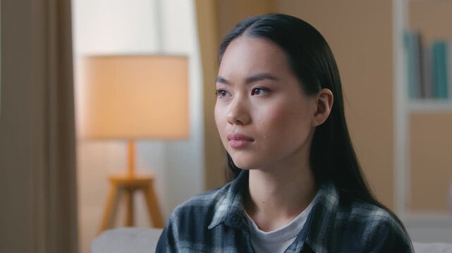 Puzzled worried Asian woman waiting pregnancy test result at home doubtful unhappy Korean Japanese female girl sitting indoors anxious unplanned baby problem unwanted children stress thinking concern