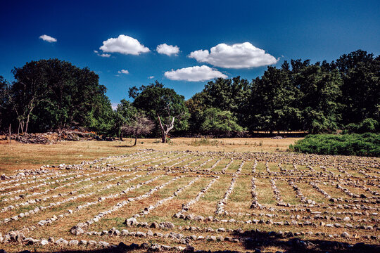View of a stone labyrinth stretches across a field of dry grass under a vibrant blue sky dotted with fluffy white clouds, Beli, Primorje-Gorski Kotar County, Croatia.