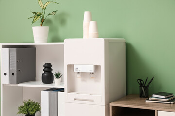Modern water cooler and shelving unit near green wall in stylish office