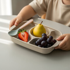 Young child in a beige shirt holding a divided silicone tray filled with a fresh strawberry, a yellow pear, and purple grapes. Generative AI.