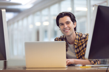 Laptop and dual monitors are sitting on desk in bright office, pens and notepad nearby