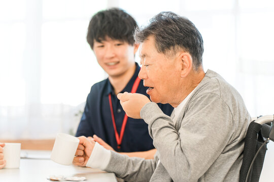 Senior man taking medicine at nursing home, male caregiver staff