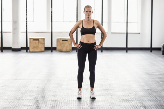 Woman standing centered in gym on rubber floor, wearing black bra and leggings near plyo boxes