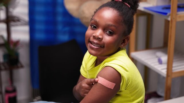 Happy African girl child proudly showing arm with plaster after vaccination in hospital