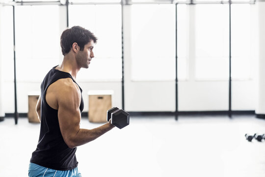 Male wearing black sleeveless top performing one-arm dumbbell curl in gym holding hex dumbbell