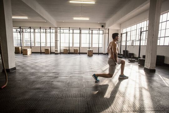Shirtless man lunging on rubber flooring at warehouse gym near plyometric boxes, copy space