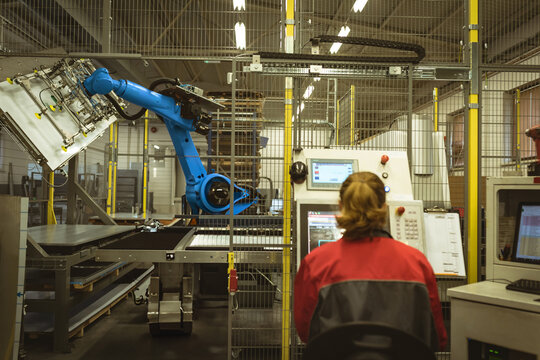 Female operator sitting at panel inputting commands and monitoring screens in factory by blue robot
