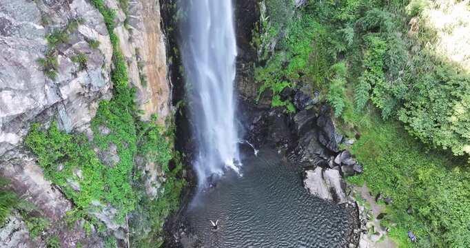 Aerial rising video of Jade Curtain Waterfall (Yu Lian Spring) in Lushan Mountain. A powerful cascade plunges into a serene pool surrounded by lush greenery and rocky cliffs. Jiangxi Province, China.