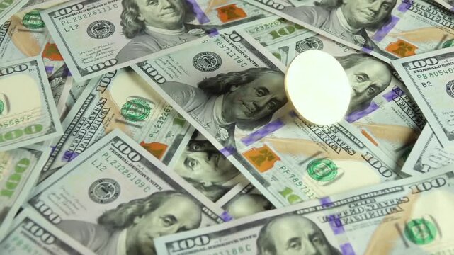 Golden cryptocurrency coin on a pile of hundred dollar bills