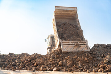 Truck tipping and unloading a pile of soil at land reclamation site.