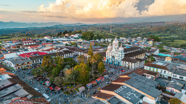 The image captures Filandia's bustling town square, showcasing colorful rooftops and the prominent church against a sunset backdrop.