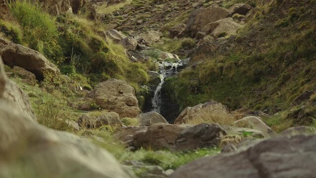 Mountain waterfall flowing through rocky Imlil landscape with green vegetation, low static establishing, nobody