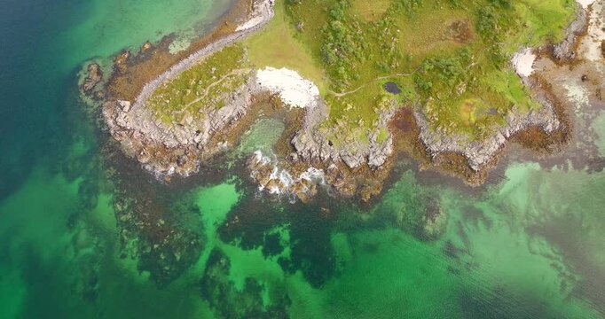 Drone shot of stunning arctic coastline at &Aring;rnessan, with clear turquoise water, rocky shores, and small sandy beach near Stokmarknes, Norway. Aerial top-down backward