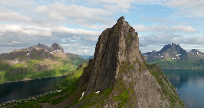 Segla mountain peak on the island of Senja, illuminated by the midnight sun, with fjords below, Norway. Aerial backward