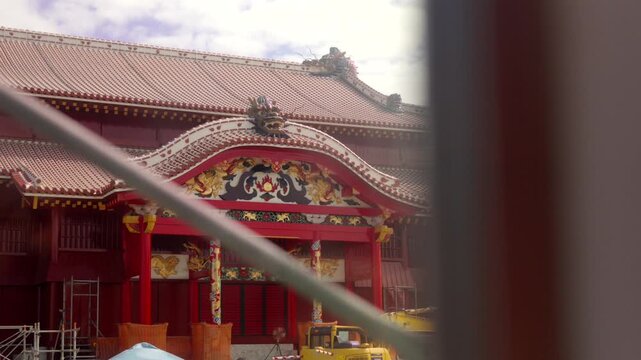 Dynamic pan shot revealing the brightly colored facade of Shurijo Castle, a UNESCO World Heritage Site in Okinawa, Japan, currently undergoing reconstruction and restoration behind protective scaffold