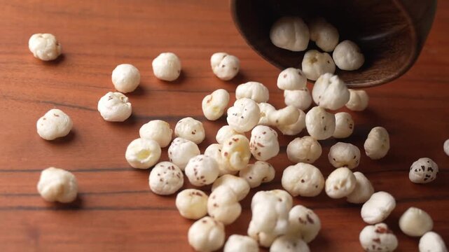 Makhana falling from wooden bowl closeup shot.