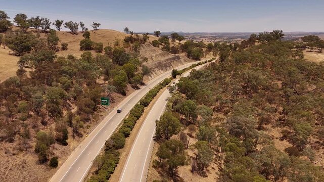 Hume Highway cutting through dry bushland with winding road and scattered trees in regional Australia, aerial approach