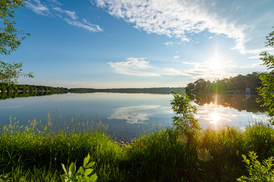 Lush green shoreline of a Waukesha County lake in early June. Bright morning sun reflects on calm Wisconsin water under blue skies.
