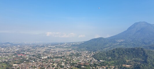 Obraz premium Panoramic view of a town surrounded by lush green mountains and clear blue sky.