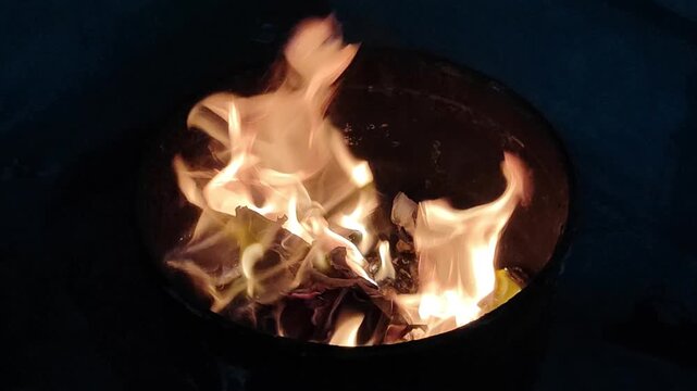 A fire burns inside a round metal container on a black background.