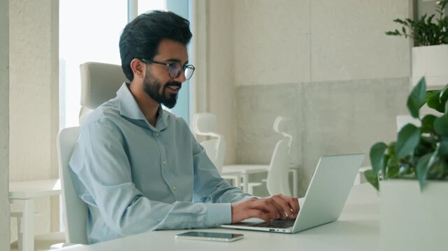 Smiling Arabian Indian business man working laptop indoors office typing email computer director male businessman guy manager entrepreneur online chatting internet work programming startup workplace