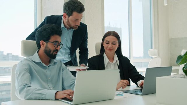Male team leader mentoring multiethnic employees reviewing work laptop indoor office boss business man supervising businesswoman Arabian businessman teamwork computer project help intern guide company