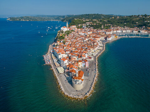 Sunny aerial view of Piran coastal town with red tiled rooftops, historic buildings and crystal blue Adriatic Sea. Popular Mediterranean travel destination in Slovenia during summer