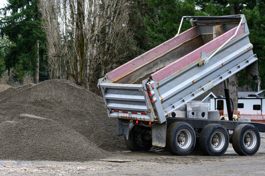 Construction dump truck unloading gravel with a hydraulic lift bed spilling material onto the ground, as a job site 
