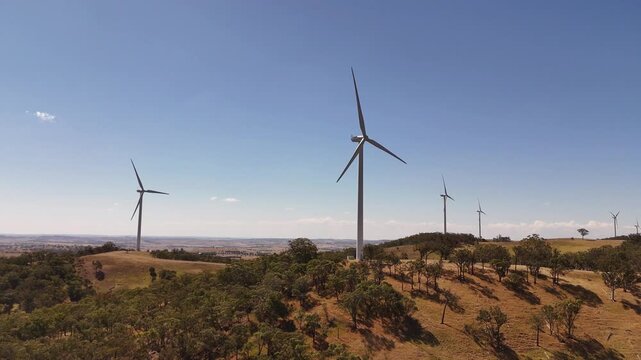 Aerial establishing of wind turbines standing on open ridgeline with vast rural horizon beyond, medium orbit