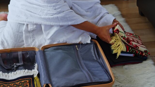 Close-up of hands pilgrim packing modest prayer mat into suitcase for Umrah or Hajj pilgrimage