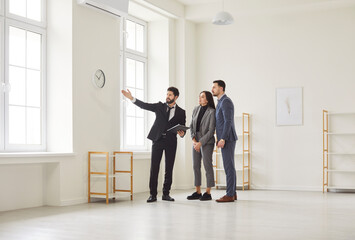 Naklejka premium Realtor showing house to a young happy couple looking at the view from the window. Professional real estate agent shows new apartment. Family ready to become homeowners. Real estate market concept.