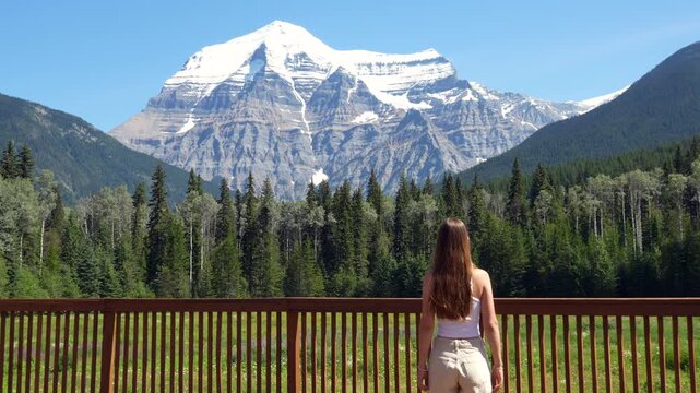 Young woman walks to the railing of an observation deck to admire the majestic Mount Robson in British Columbia, Canada.